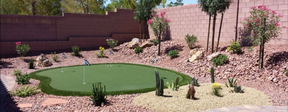 An enclosed backyard with a putting green, trees, and shrubbery.