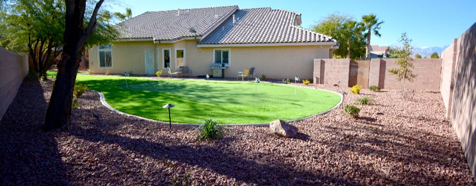 Backyard of a Las Vegas home, featuring a turf yard surrounded by rock and pavers.
