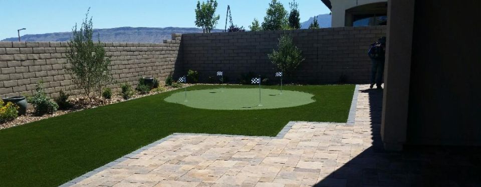 A backyard with an artificial turf golf course that combines nicely with pavers for a patio extension.