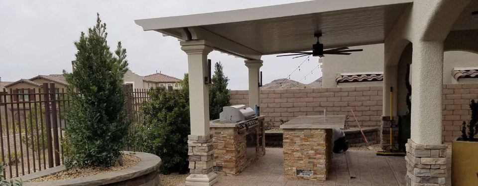 An outdoor kitchen covered by a patio cover that fits in with the landscape design.