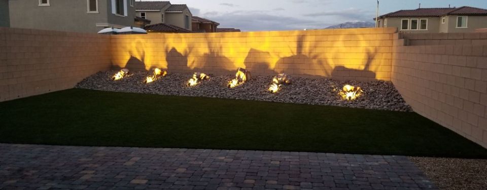 A well-landscaped yard at dusk with landscape lighting lighting up the area.